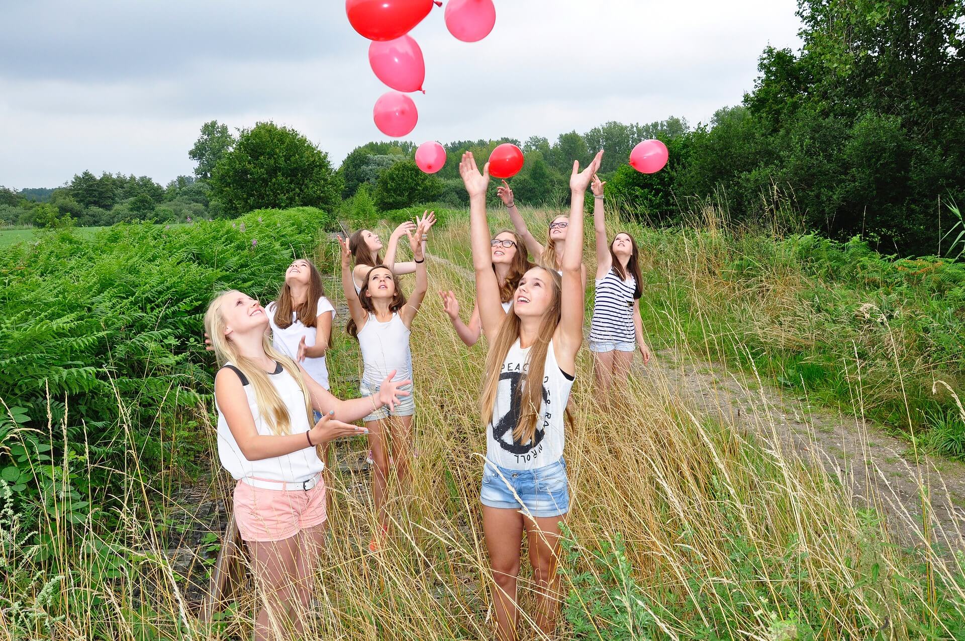 Eine Gruppe von Mädchen werfen rosa Ballons in die Luft