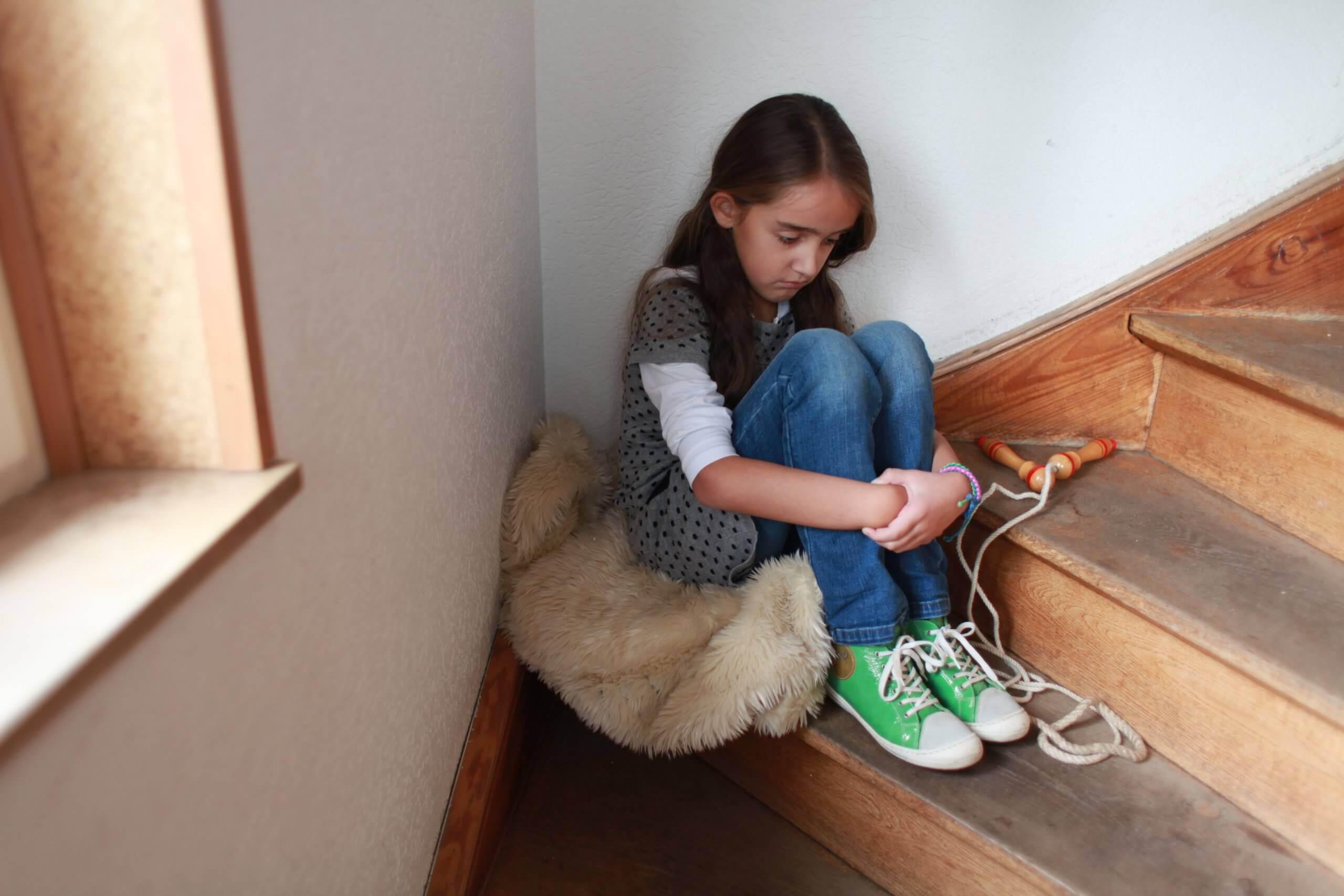 Ein Mädchen sitzt traumatisiert auf einer Holztreppe